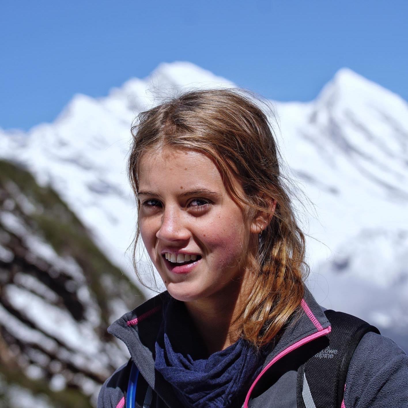 Gabby smiles at the camera. Tall white mountains loom in the background.